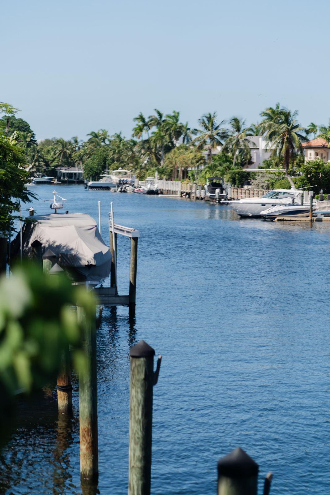 A Pompano Beach residential canal with wooden docks, covered boats, and palm trees along the banks.